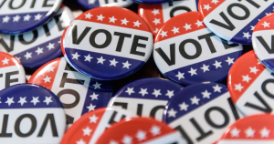 Several lapel pins with the word "VOTE" written on them and decorated with red and blue colors, as well as white stars.